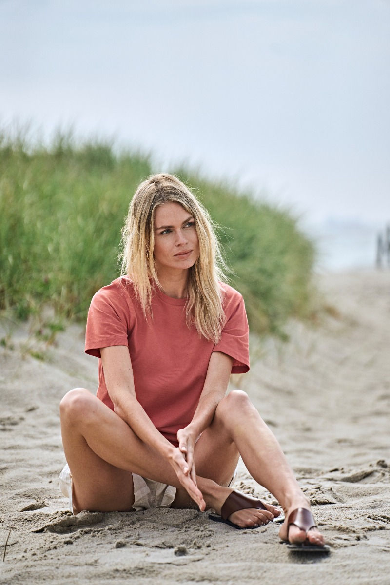 Woman in a red Tee Jays Label Free t-shirt sitting on the beach sand.